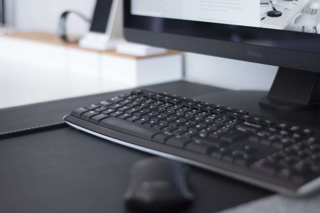 Poste de travail de bureau : écran, clavier et souris posés sur un sous-main noir